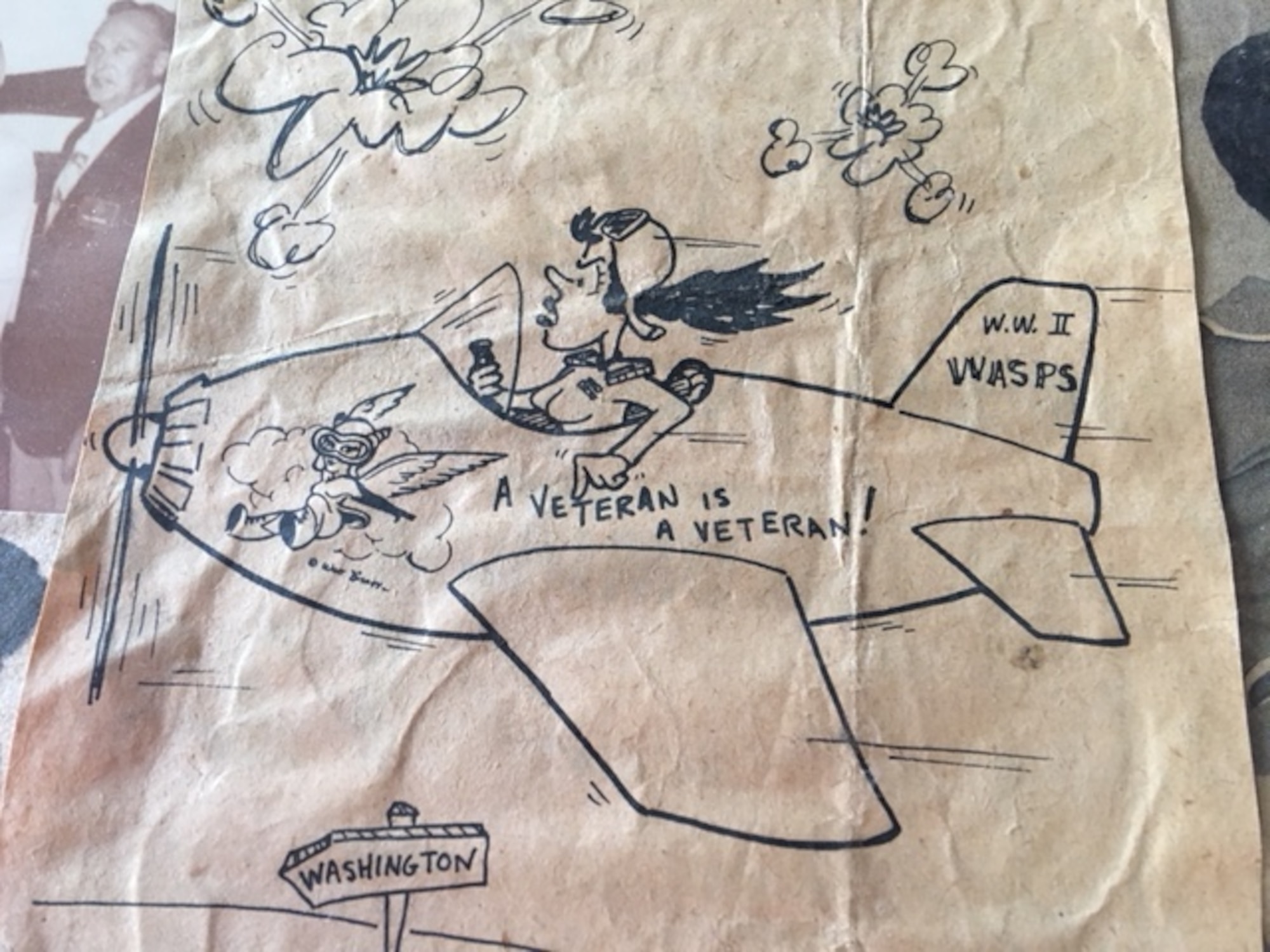 drawing of a WASP in an aircraft flying to Washington with the words WWII WASPS on the tail and the words A Veteran is a Veteran! on the side of the aircraft.