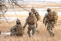 A group of uniformed personnel walk through a field with their weapons.