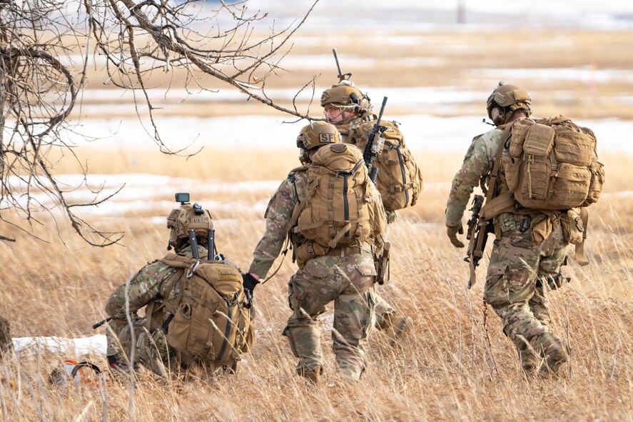 A group of uniformed personnel walk through a field with their weapons.