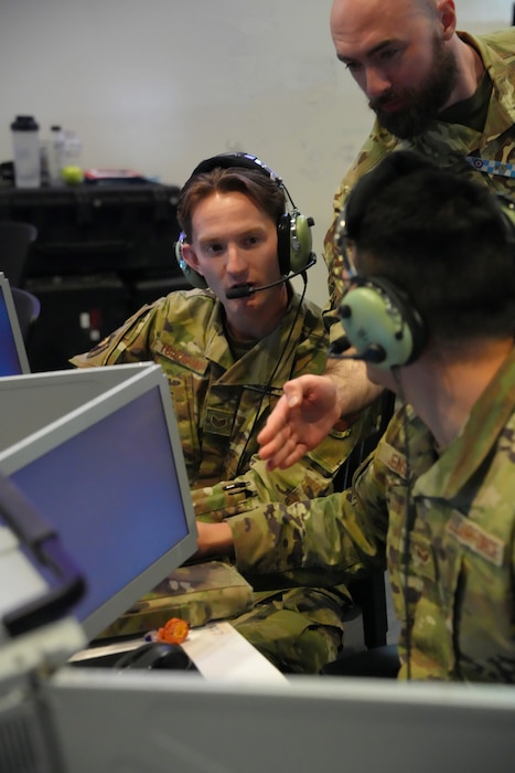 photo of US and UK military members wearing headsets work on computers