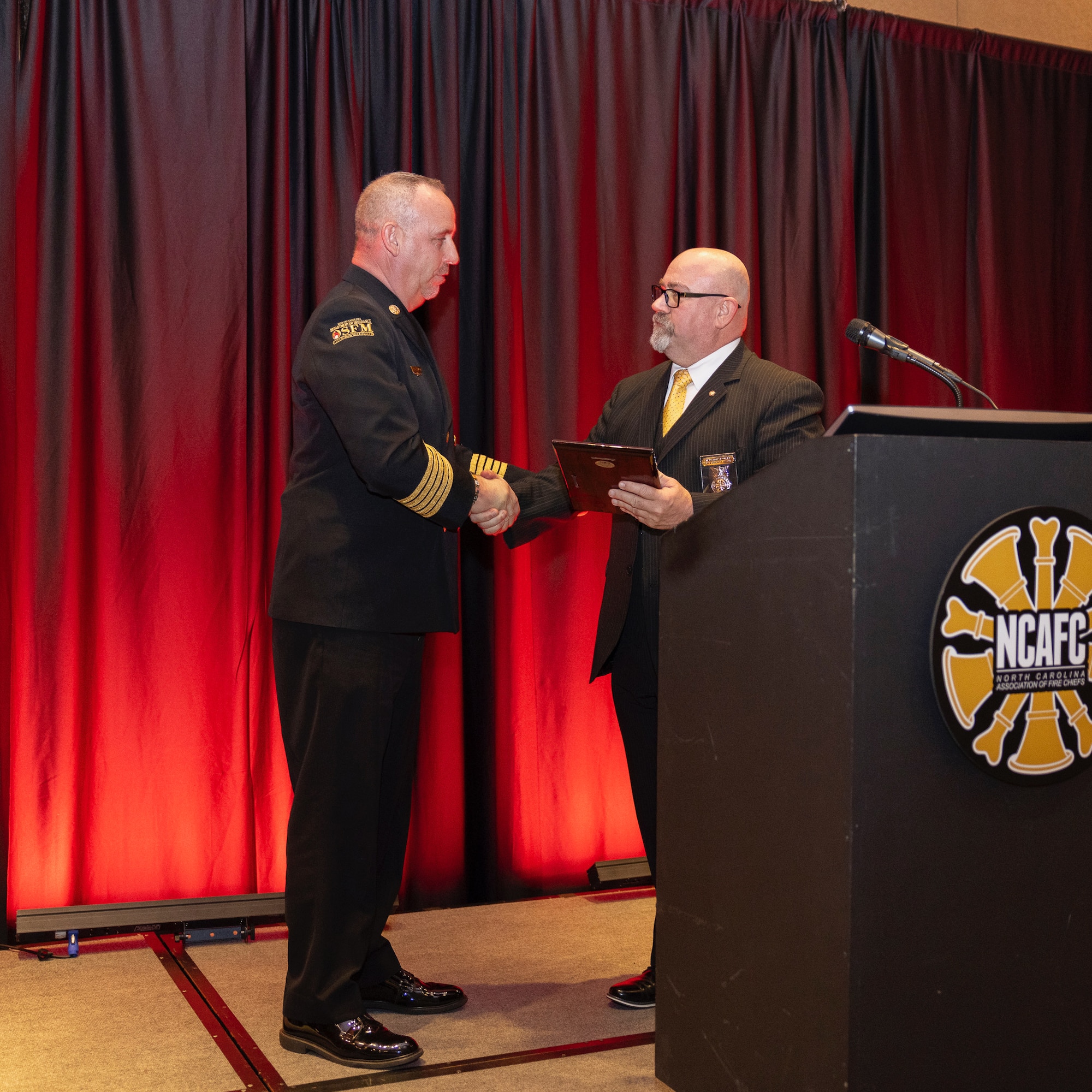 Chief Charles B. Loveday, Air National Guard command fire chief, right, presents Brian Taylor, North Carolina State Fire Marshal with a plaque in recognition of an ongoing partnership with the 145th Airlift Wing at the Mid-Winter Fire Chiefs Conference banquet at the Embassy Suites in Concord, N.C., Jan. 31, 2025.