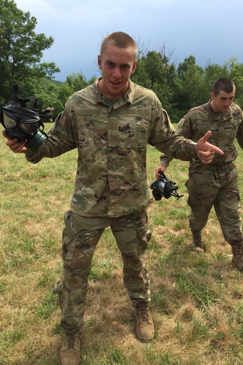 Two soldiers stand in a field holding masks.