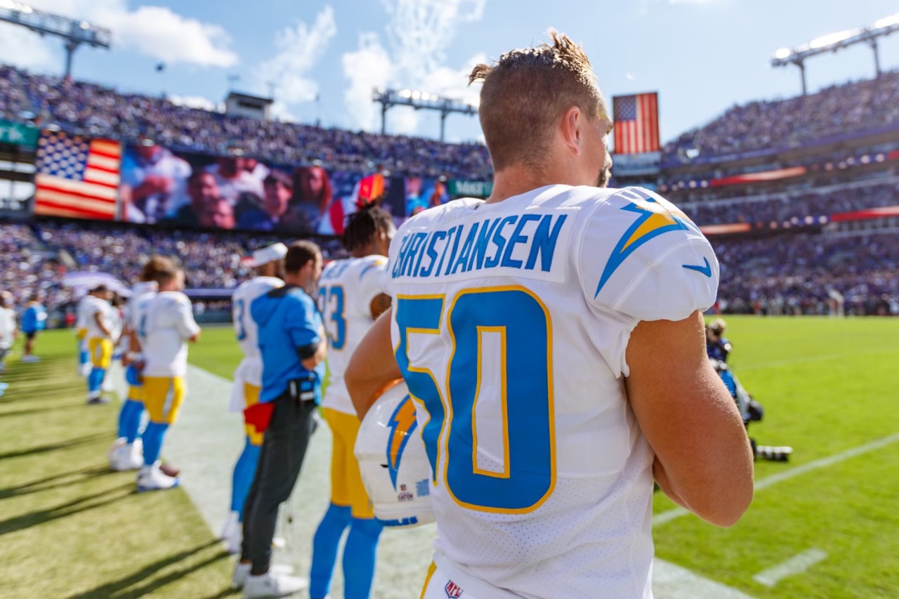 Football players stand on the sideline of a football field.