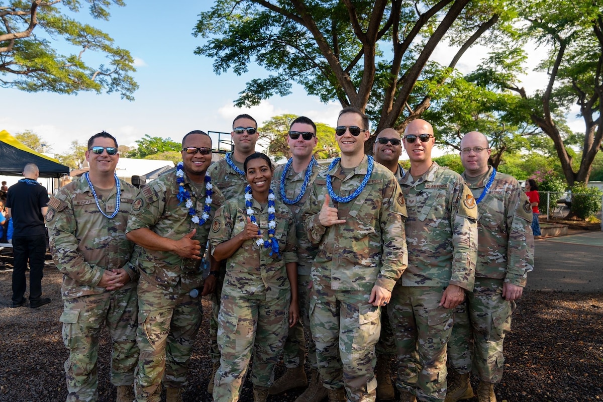 9 uniformed soldiers with flower necklaces pose together for a photo outdoors.