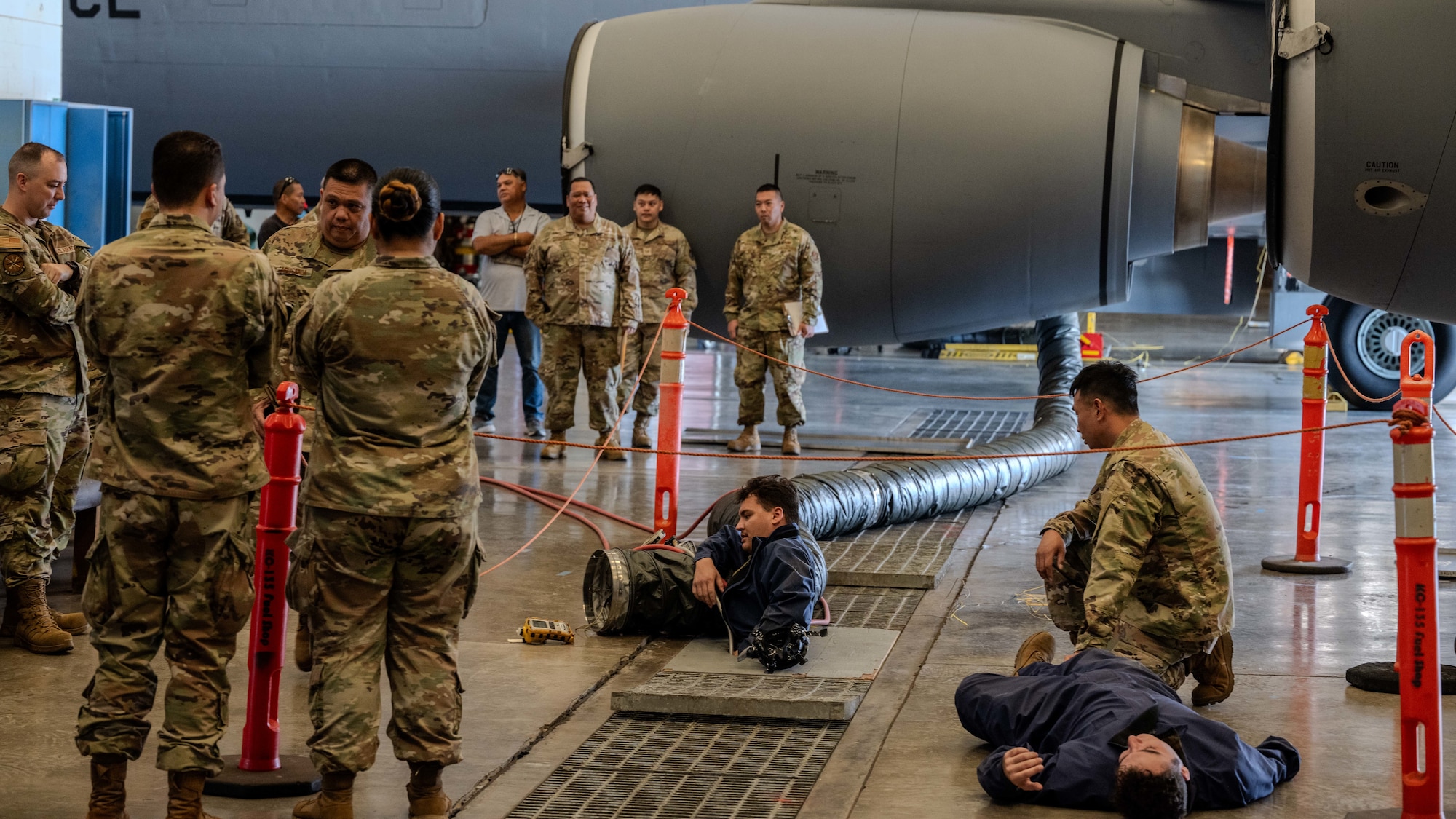 An Airman is exiting a hole that is located in the ground while the simulated patient is lying next to the opening.