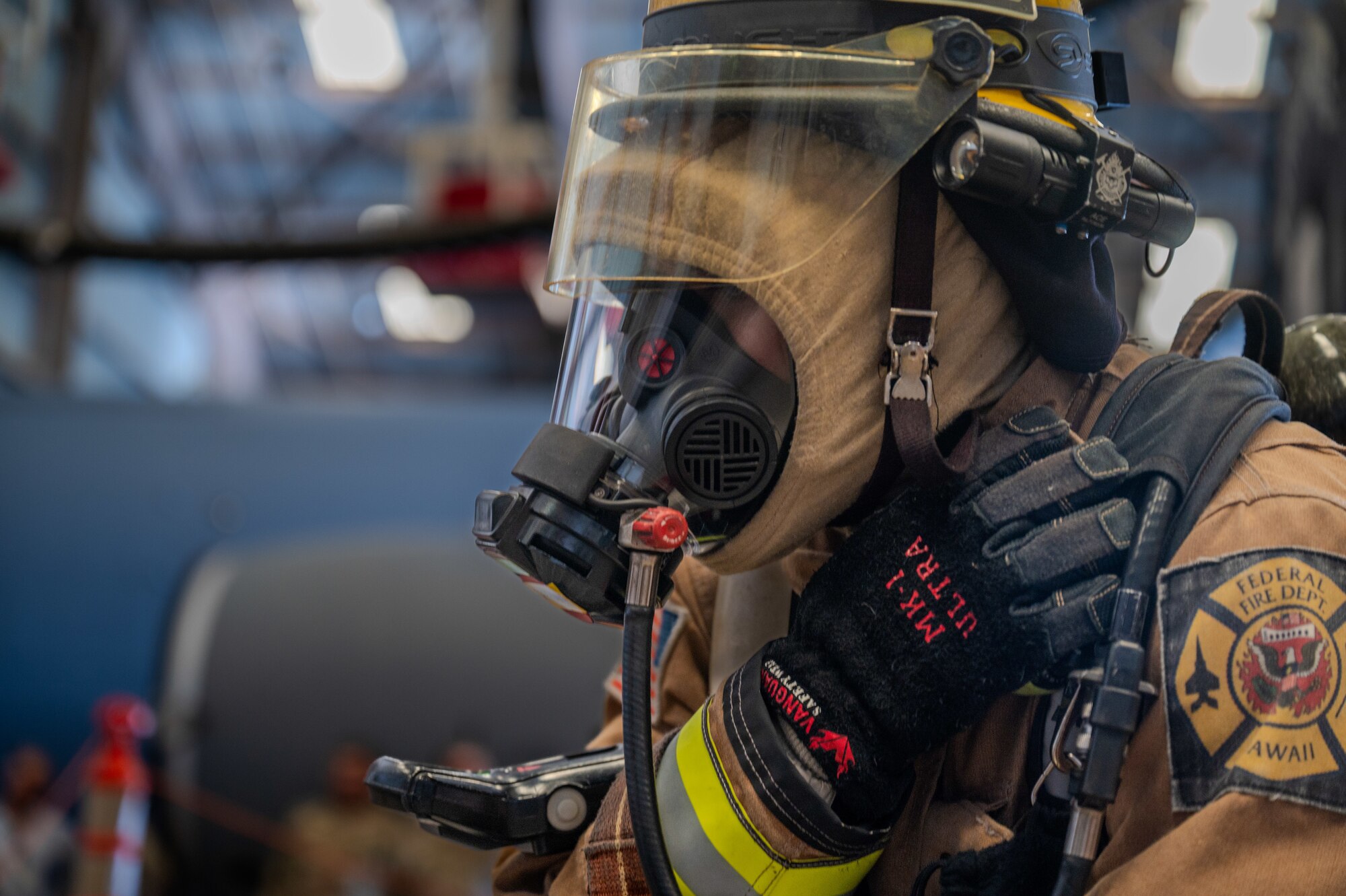 A firefighter uses his hand to operate a walkie talkie that is located on his shoulder.
