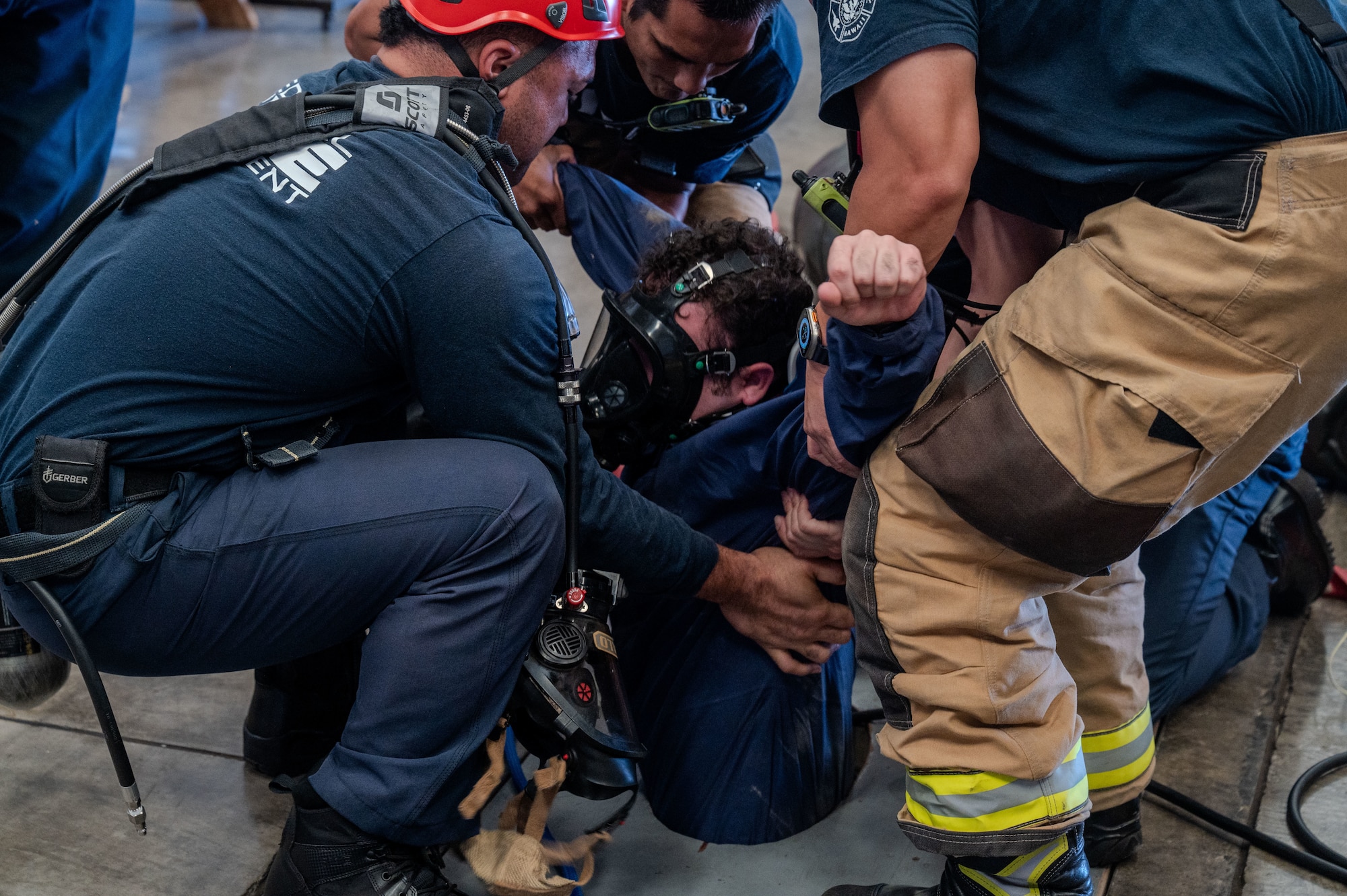 three firefighters gathered around an opening pull an Airman out of a hole.