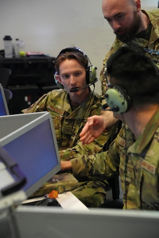 photo of US and UK military members wearing headsets work on computers