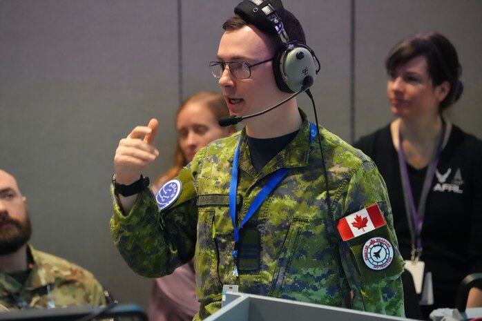 Coalition member wearing headset standing up talking while others behind him listen
