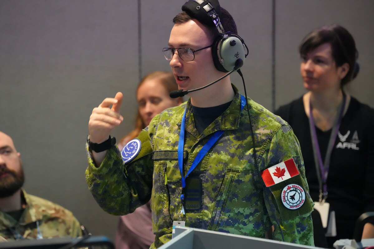 Coalition member wearing headset standing up talking while others behind him listen