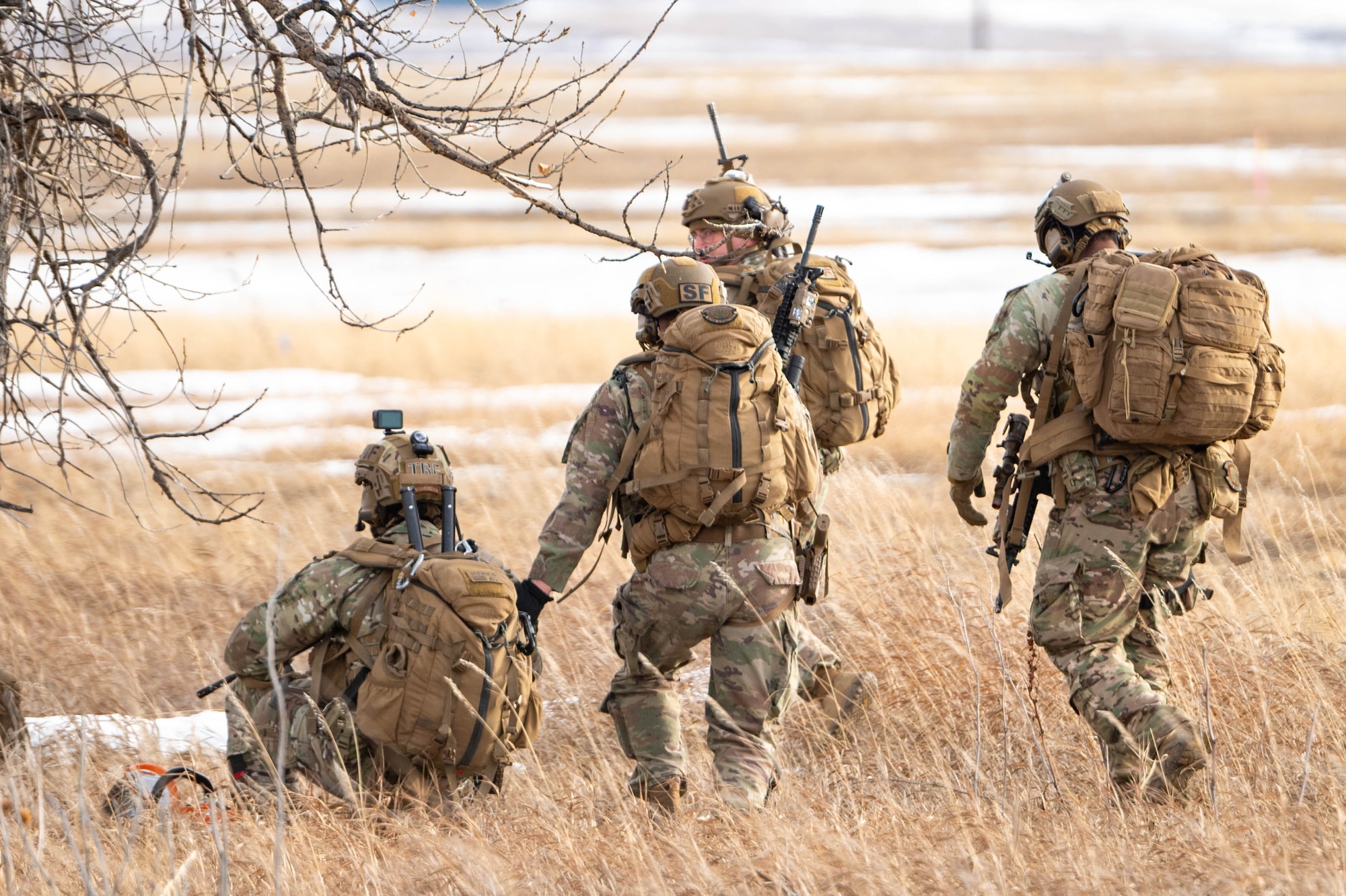 A group of uniformed personnel walk through a field with their weapons.