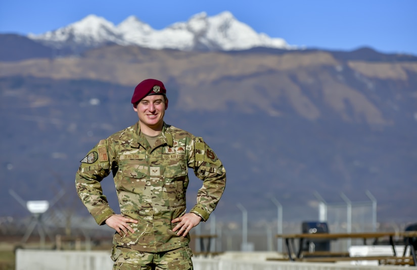 An airman poses for photo in military gear in front of towering mountains in the background.