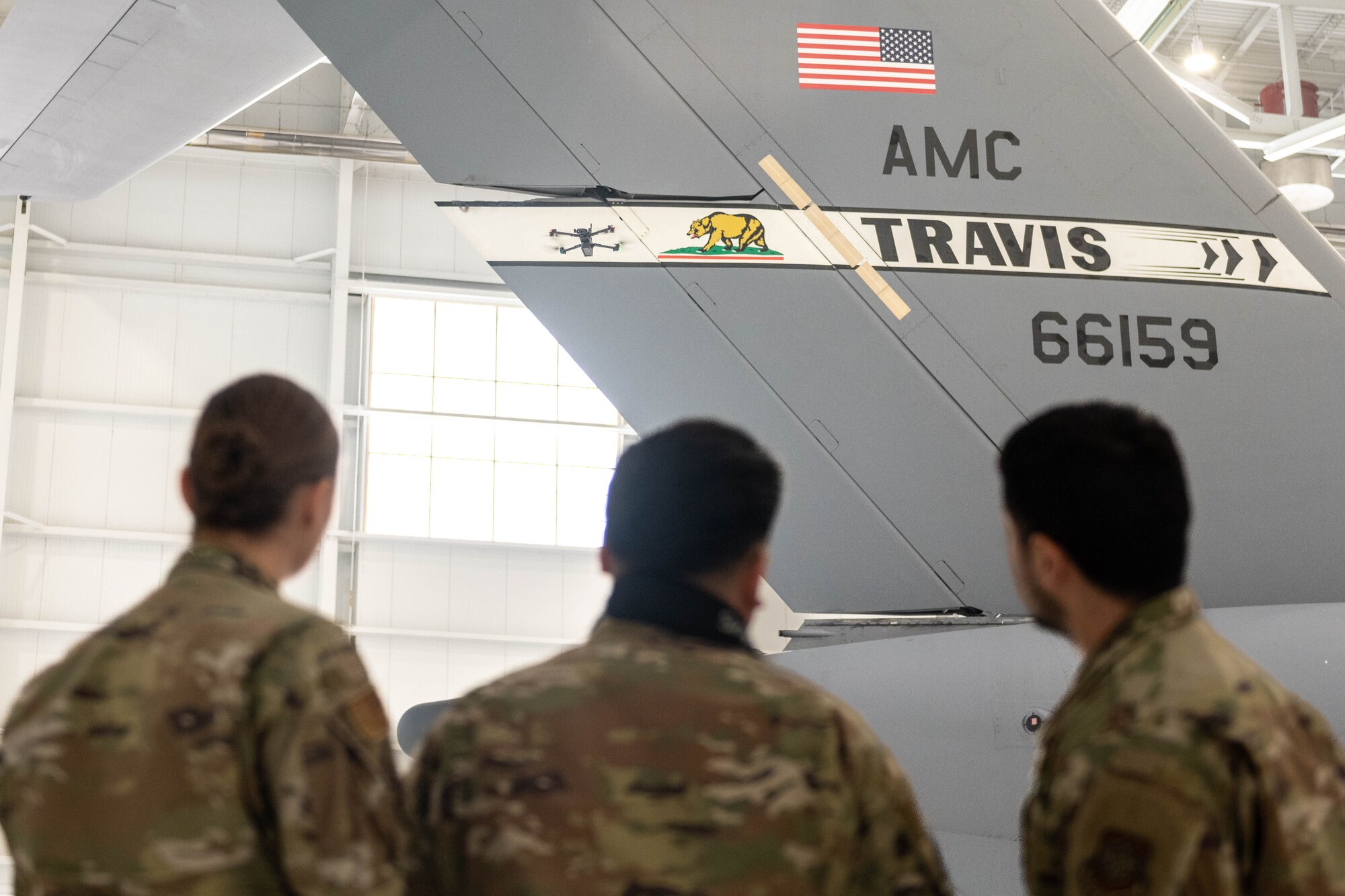 Three Airmen are seen from behind as they look at the t-tail of a plane