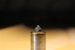 Pictured is all that remains of a 1-mm tapered tungsten rod held by a graphite holder after being bombarded by 5 kilojoules of 2.5 million volt electrons in only 50 nanoseconds. The rapid deposition of energy is cylindrically-symmetric and vaporizes most of the 5-cm long rod, leaving behind a single, tiny tungsten “flower.” This debris was made during our studies of high-brightness radiographic diodes. The NRL-patented rod-pinch diode provides one of the world’s brightest hard x-ray sources and is used to characterize material properties under dynamic loads, supporting the Nation’s nuclear stockpile. Experiments were supported by the Department of Energy National Nuclear Security Agency under Interagency Agreement DE-NA-0001417. (U.S. Navy photo)
