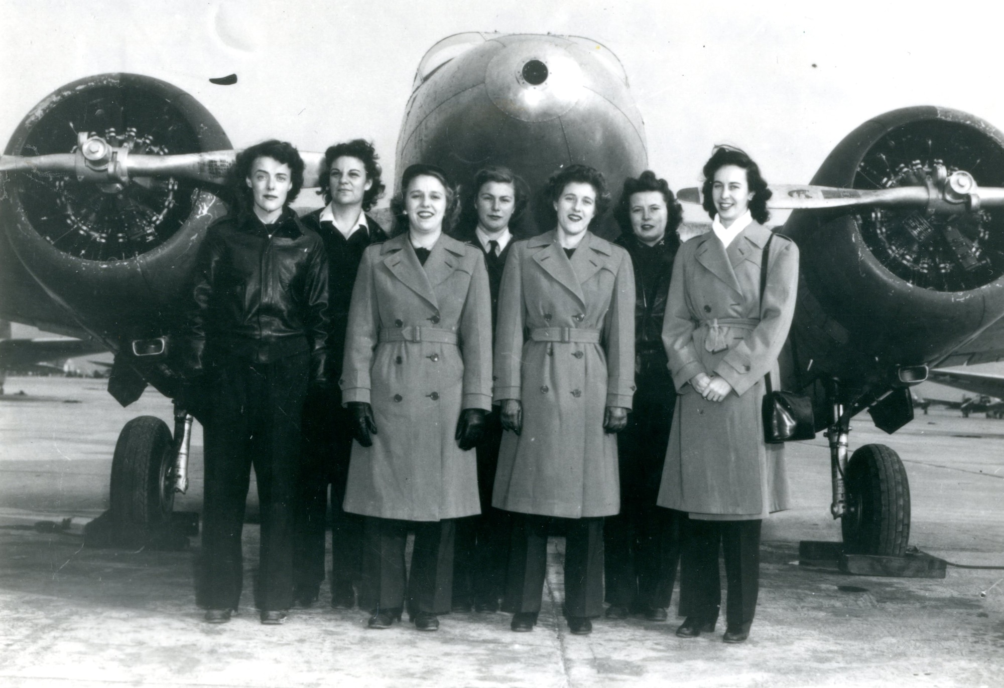 Seven WASP dressed in long coats, some wearing gloves, standing in front of an AT-10, stationed at Freeman Army Airfield in Fall 1944.