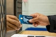 A Fort Jackson Army Military Pay Office military pay technician hands a new EagleCash card to an Army Basic Combat Training trainee at Fort Jackson, South Carolina, April 20, 2022. EagleCash is a stored value card that serves as a cash management tool where funds are loaded to a card and linked to the cardholder's personal account at a financial institution, using a self-service kiosk. (U.S. Army photo by Mark R. W. Orders-Woempner)