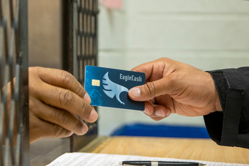A Fort Jackson Army Military Pay Office military pay technician hands a new EagleCash card to an Army Basic Combat Training trainee at Fort Jackson, South Carolina, April 20, 2022. EagleCash is a stored value card that serves as a cash management tool where funds are loaded to a card and linked to the cardholder's personal account at a financial institution, using a self-service kiosk. (U.S. Army photo by Mark R. W. Orders-Woempner)