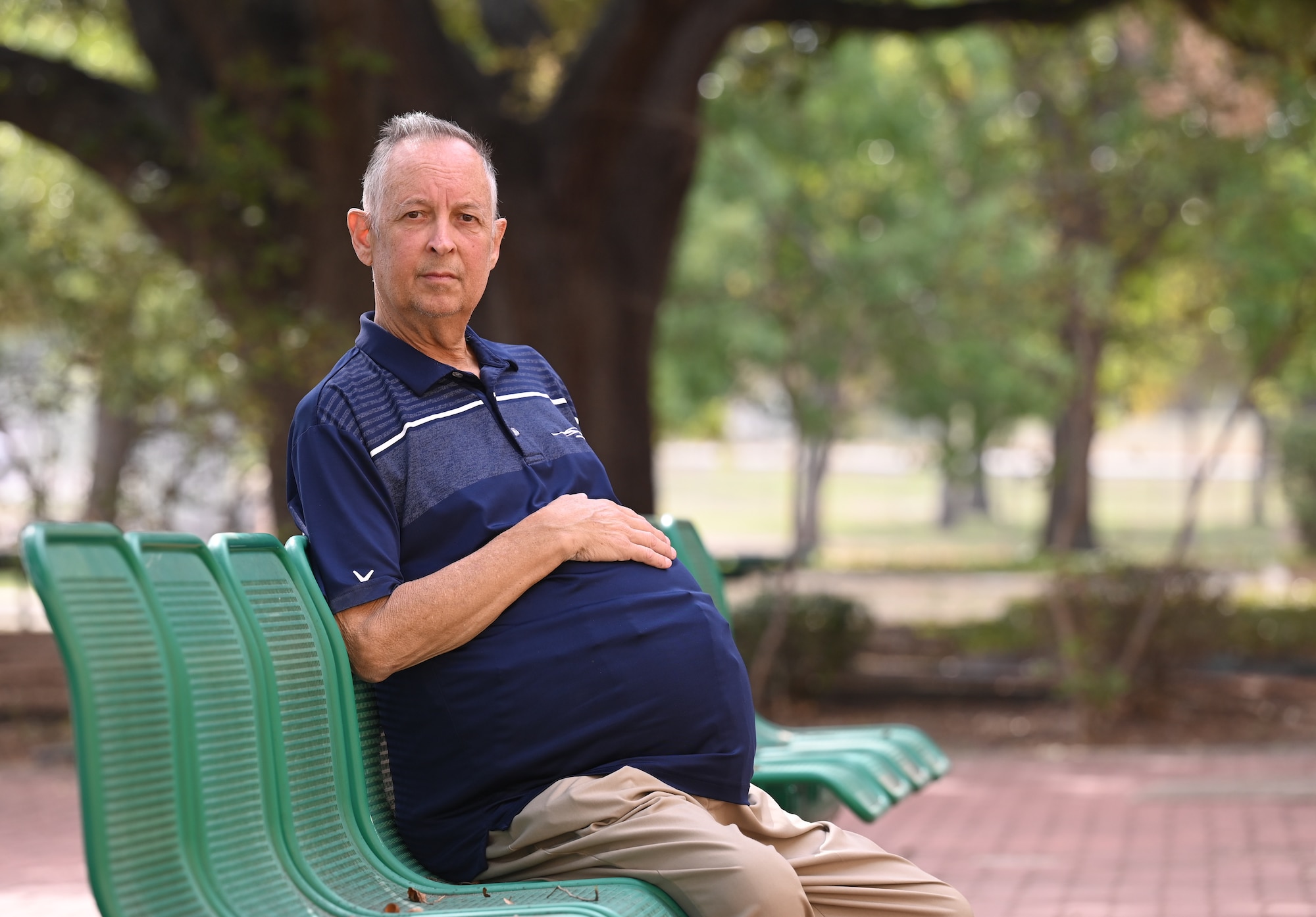 A gentleman with an over-sized mid section due to polycystic disease, sits in an outside break area.