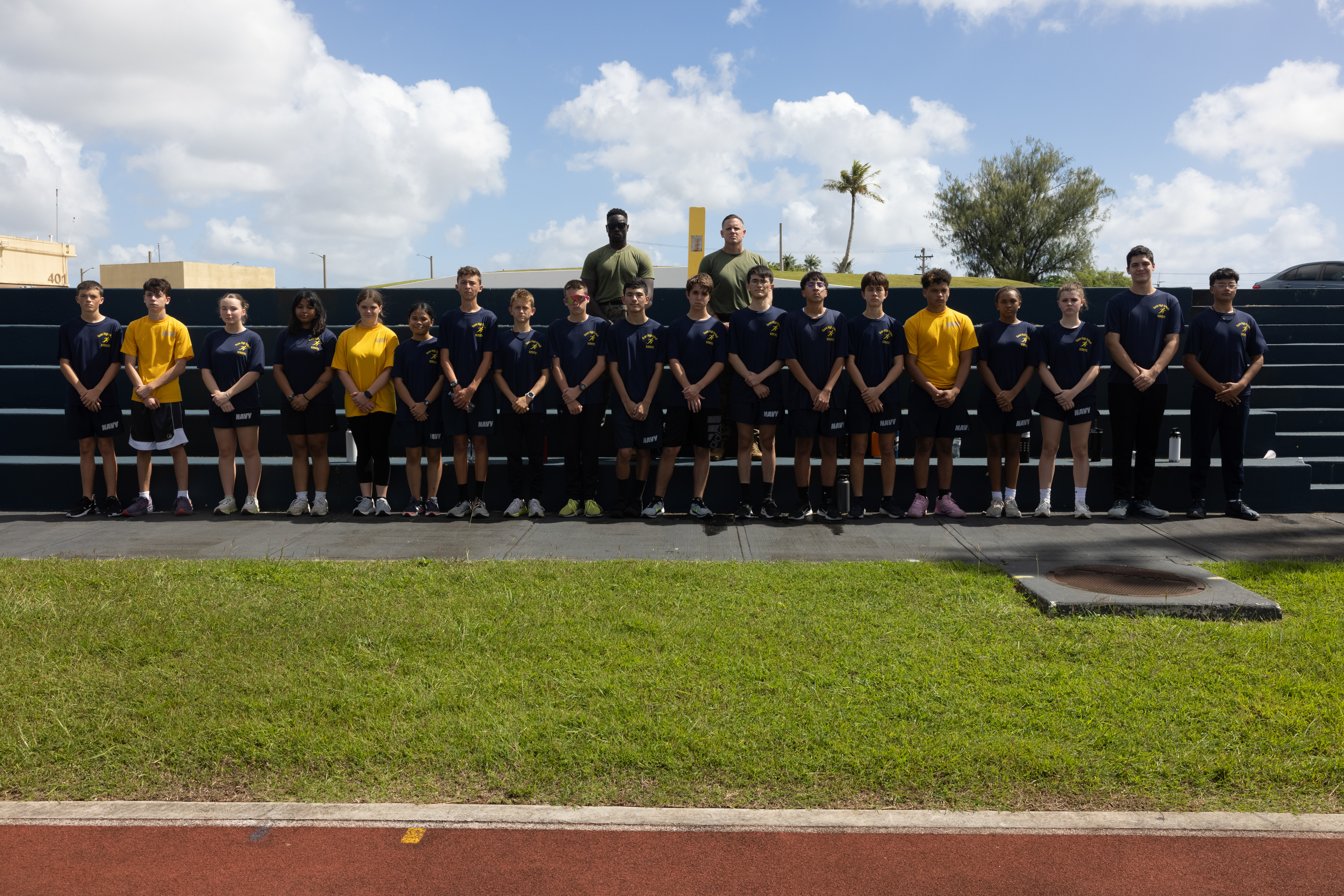 U.S. Marine Corps Sgt. Davis Williams, maintenance administrative specialist, Headquarters Company, Marine Corps Base Camp Blaz, and Gunnery Sgt. Karl Benton, training chief, Headquarters Company, MCB Camp Blaz, pose with Navy Junior Reserve Officers' Training Corps students after a combat fitness test at Guam High School, Guam, Jan. 23, 2025. Marines with MCB Camp Blaz partnered with the Guam High School NJROTC program to conduct mock CFTs for the students so they could better understand fitness requirements of the military. (U.S. Marine Corps photo by Cpl. Ryan Little)