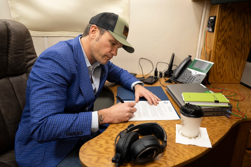 Defense Secretary Pete Hegseth signs a memorandum at a desk aboard an aircraft.