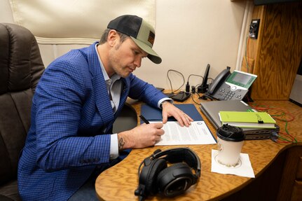 Defense Secretary Pete Hegseth signs a memorandum at a desk aboard an aircraft.