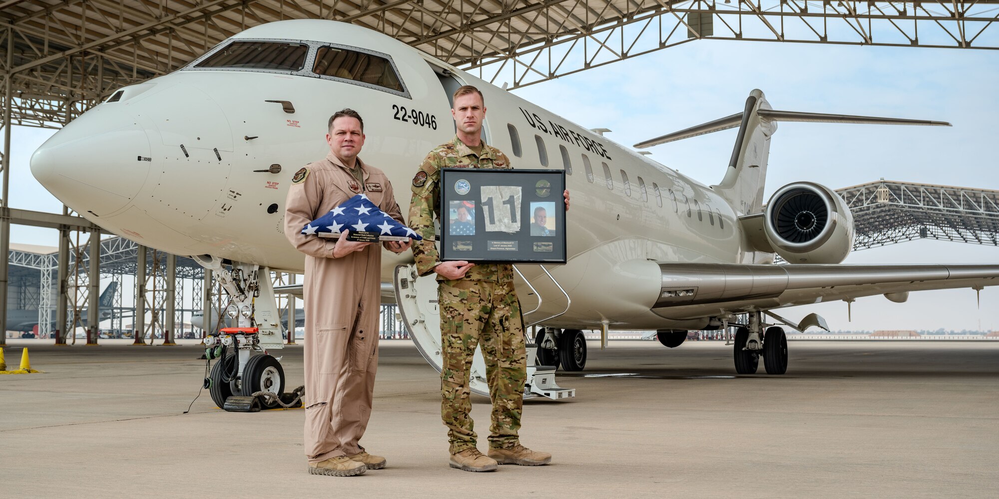 U.S. Air Force Lt. Col. Randell McCart, the 430th Expeditionary Electronic Combat Squadron commander, and Maj. Eric Goodman, a 430th EECS E-11A pilot, hold up a memorial dedicated to two fallen E-11 A pilots in the U.S. Central Command area of responsibility, Jan. 27, 2025, marking the 5th anniversary of an E-11A crash that claimed the lives of two 430th EECS pilots, Lt. Col. Paul “Tabs” Voss and Capt. Ryan “Fogg” Phaneuff.