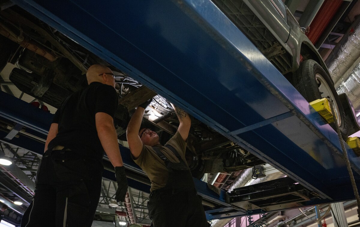 Two vehicle maintainers look up under a raised vehicle