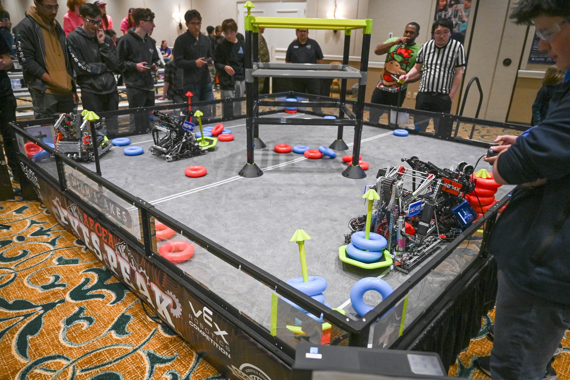 Participants stand around the arena as their robots collect rings in the match.