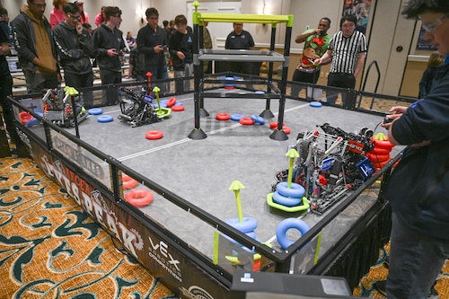 Participants stand around the arena as their robots collect rings in the match.