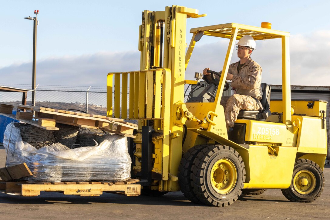 A Marine operates a yellow forklift carrying supplies.