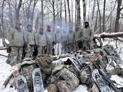 A team of Air National Guard Airmen stand in front of a thermal shelter built using limited supplies and materials found in nature during the Air National Guard's Cold Weather Operations Course at Camp Ripley Training Center, Minn., Feb. 4, 2025.