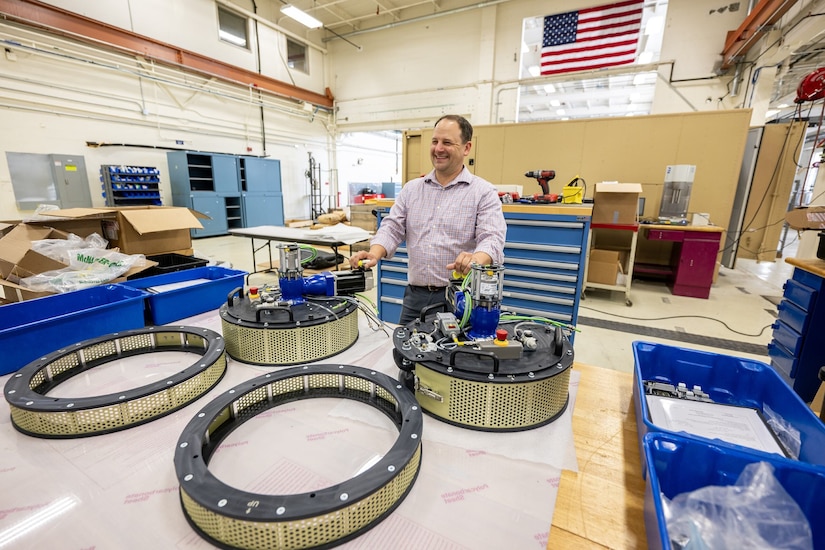 A man puts his hands on two round motorized pieces of equipment sitting on a table.