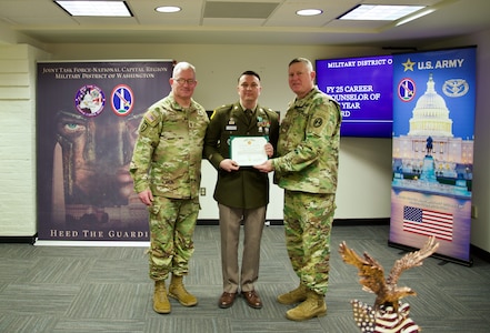 A Soldier dressed in Army green service uniform is holding a certificate and posing for a picture with two soldiers on either side of him.