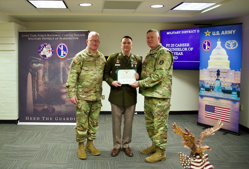 A Soldier dressed in Army green service uniform is holding a certificate and posing for a picture with two soldiers on either side of him.