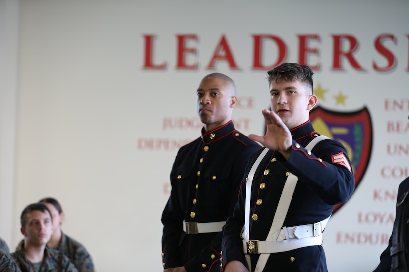 Two Marines are talking, and one is gesturing with his hand while talking. Behind them on the wall it reads "Leaders."