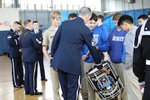 An Air Force Airman is leaning over to show high school students a drum. They are in a gymnasium.