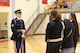 An Army soldier dressed in ceremonial uniform and holding a rifle is talking with students in a gymnasium.