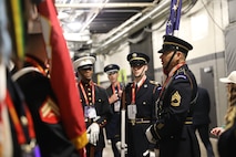 Service members in ceremonial uniforms are talking in a hallway at Caesars Superdome just before they present the colors on the field for the Super Bowl.