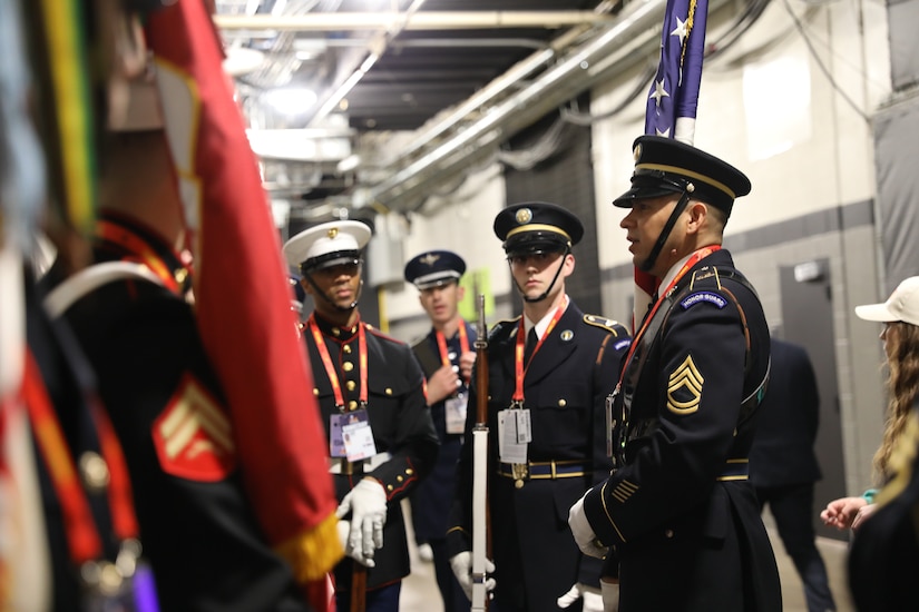 Service members in ceremonial uniforms are talking in a hallway at Caesars Superdome just before they present the colors on the field for the Super Bowl.