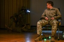 An airman sits in a chair acting as a hostage