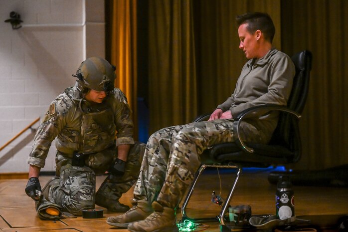 An Airman examines a mock explosive device under the acting hostage during a hostage rescue training exercise