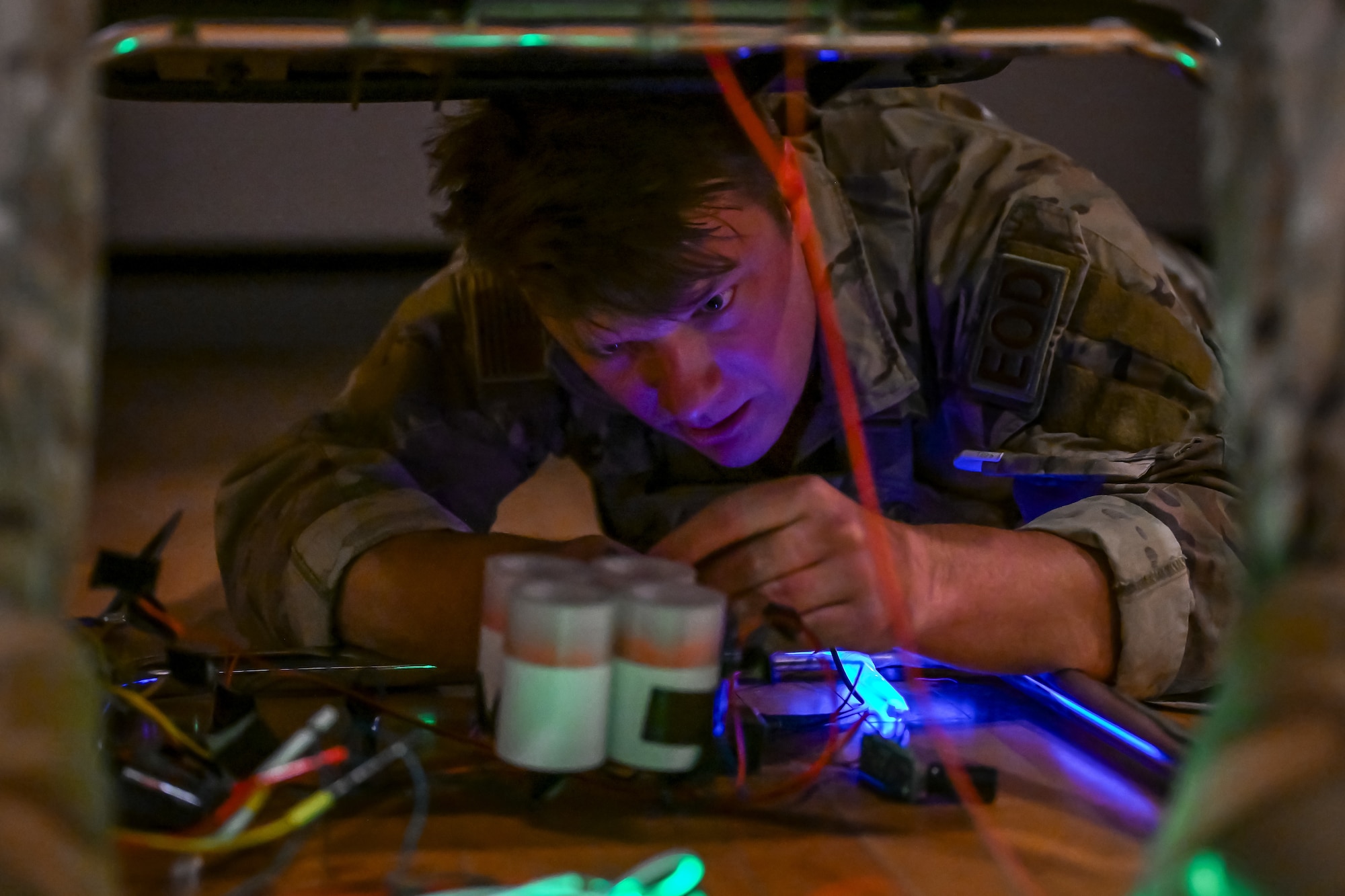 An Airman from EOD works on dismantling a simulated explosive under a hostage on a chair