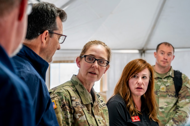 Three civilians and two army soldiers speak in a white tent.