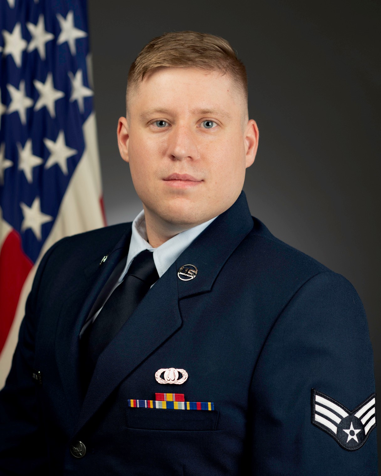 Official photo of SrA Andrew Compton with the American flag behind him. He is wearing his service dress.