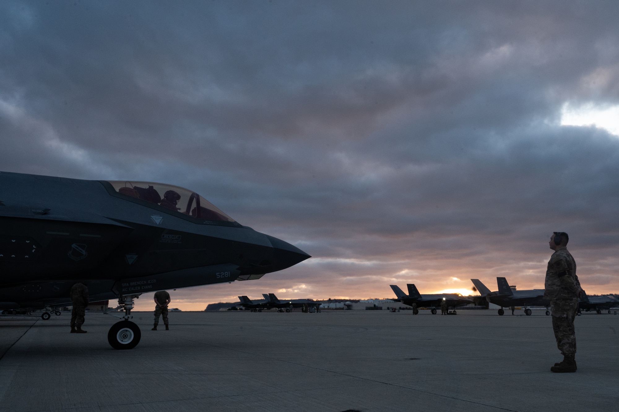 A photo of a maintainer standing in front of an F-35A Lightning II at sunset