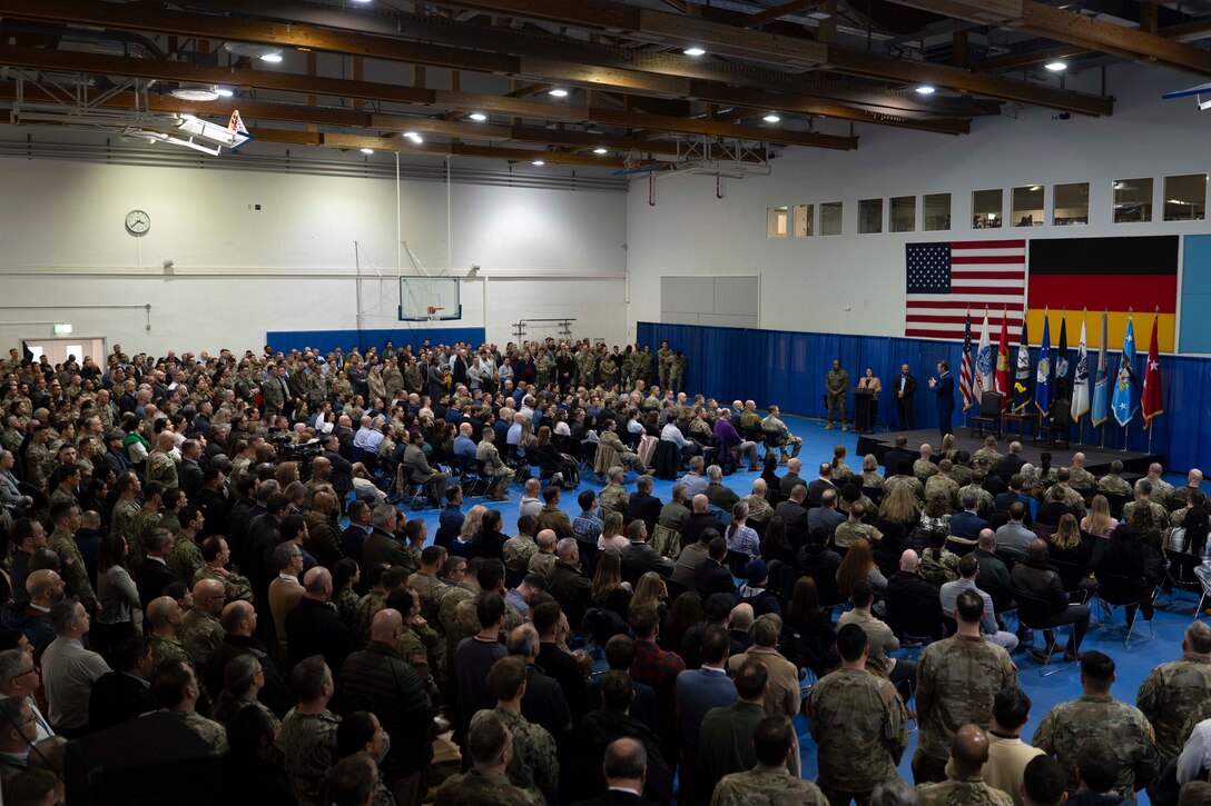 A large audience looks toward a stage with flags.