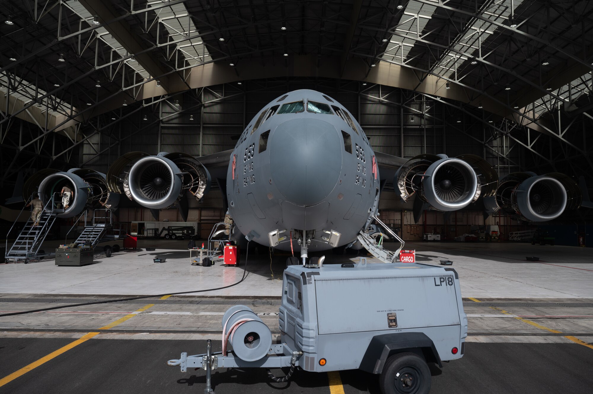 A C-17 Globemaster is parked in a Hangar with a generator parked in front of it.