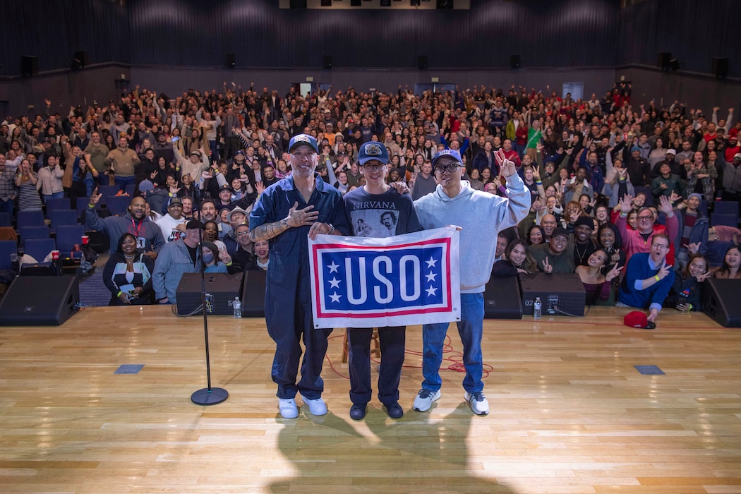 Comedian Jo Koy, his son, and DJ Turbulence pose with a USO banner in front of the audience at the end of the performance at the Morale, Welfare and Recreation (MWR) Fleet Theater at Commander, Fleet Activities Yokosuka.