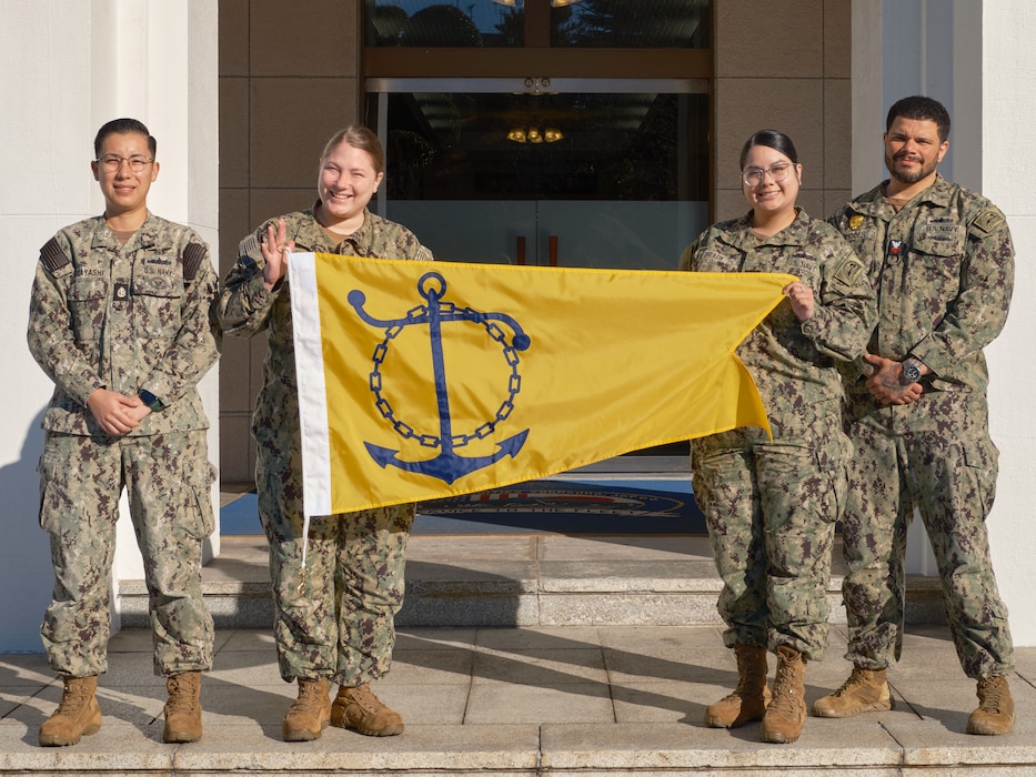 Staffmembers from the Commander, Fleet Activities Yokosuka (CFAY) Command Career Counselors' Office (from left to right) Chief Navy Counselor Daniela Kobayahsi, Boatswain's Mate 2nd Class Tiffany Steirs, Operations Specialist 2nd Class Karyssa Brady, and Master-at-Arms 1st Class Charlie Rhodes pose outside the command's headquarters building with the Navy Retention Excellence Award Pennant Friday, January 31, 2025.