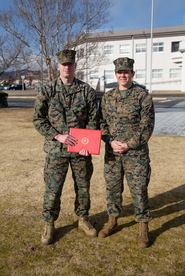 U.S. Marine Corps Lance Cpl. Brandon Champagne, left, an air traffic controller with Headquarters and Headquarters Squadron, Marine Corps Air Station Iwakuni, and a Florida native, poses for a photo with Maj. Kate Herren, the air traffic control facilities officer with H&HS, MCAS Iwakuni, and a Washington native, after a Navy and Marine Corps Achievement Medal award ceremony at MCAS Iwakuni, Japan, Jan. 29, 2025. Lance Cpl. Champagne received the Navy and Marine Corps Achievement Medal for rescuing two individuals trapped in wreckage after a vehicle accident while home on leave. (U.S. Marine Corps photo by Cpl. Colin Thibault)